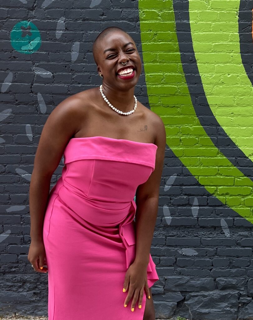 Ivana, a Black woman, is wearing a hot pink strapless dress. She's laughing and smiling big looking at the camera